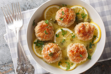 Chicken meatballs are finished with a velvety piccata sauce complete with lemon, white wine, and capers closeup on the plate. Horizontal top view from above