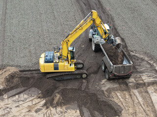 Excavator loads earth on a construction site onto a tractor with dump truck, civil engineering, road construction, landscaping, earthworks