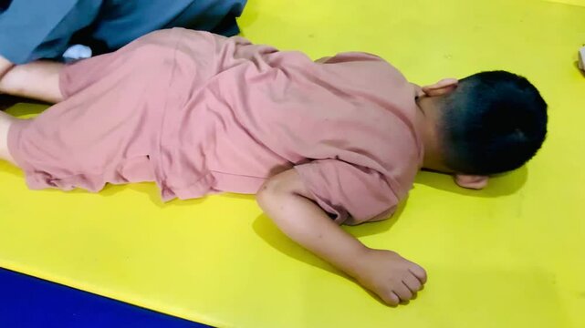 A caring female physiotherapist gently performs neuromuscular stimulation therapy on a child with cerebral palsy in the hospital&rsquo;s physiotherapy room. The child lies comfortably on his stomach.