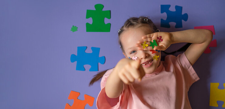 A girl with a lot of pieces of colorful puzzles in hand points finger forward. Banner on education and awareness about autism