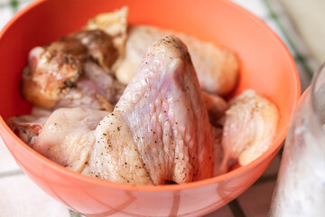 Chicken wings in a bowl sprinkled with coarse salt and black pepper. The wings appear fresh and are ready for marination. The seasoning. Preparation for cooking. Hight quality photo