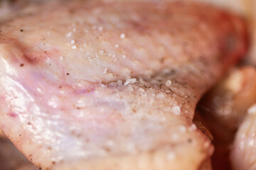 Fototapeta premium Chicken wings in a bowl sprinkled with coarse salt and black pepper. The wings appear fresh and are ready for marination. The seasoning. Preparation for cooking. Hight quality photo