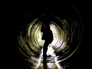 A silhouette of a traveler stands inside a dark tunnel, water reflects light as they explore this hidden urban space and embark on an intriguing adventure