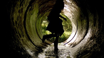 A person is running through a dark tunnel, illuminated by soft light from the opening. Water flows beneath their feet, merging excitement with exploration in a natural setting
