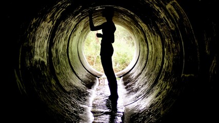A silhouette stands at the entrance of a dark tunnel, surrounded by water with sunlight streaming in. This moment captures the thrill of adventure and exploration in an urban environment