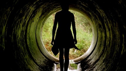 A figure stands silhouetted at the entrance of a dark tunnel, surrounded by greenery. The exploration of this unique spot promises adventure beneath the surface of nature's beauty