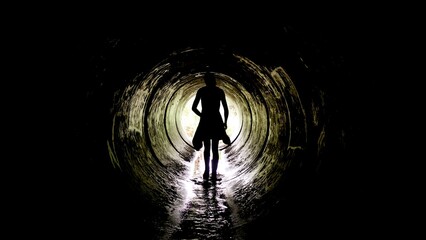 A silhouette stands in a moist underground tunnel, water reflecting light as it flows beneath bare feet. This exploration showcases the thrill of discovering hidden places