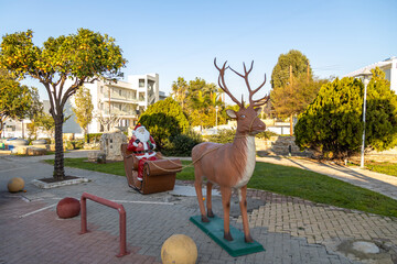 Xmas installation of Santa Claus on a reindeer sleigh among green trees in sunny winter Cyprus....
