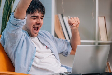 Obraz premium young man or student sitting indoors with laptop and euphoric expression of success
