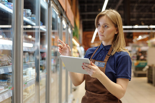 Waist up portrait of female supermarket worker holding digital tablet and doing stock review control, copy space
