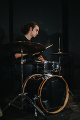 A drummer focuses intensely while performing on a drum set during a band rehearsal.