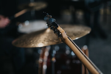 Musical instruments captured with a focus on a guitar neck, featuring drums blurred in the...