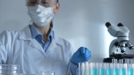 Scientist woman, wearing a lab coat, mask, blue gloves and safety glasses, is using a micropipette...