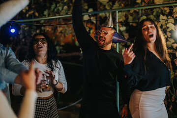 A group of cheerful friends engage in a lively party outdoors at night, donning fun accessories and...