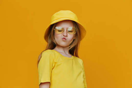 A cheerful girl in a bright yellow outfit and sunglasses poses playfully against a sunny yellow background, exuding summer vibes and youthful energy