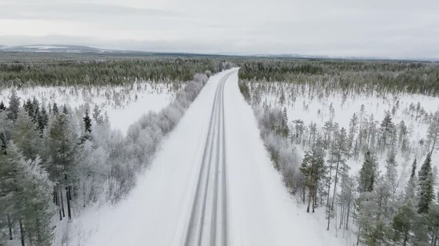 Plan a&eacute;rien reculant au dessus d'une route vide de campagne enneig&eacute;e au milieu d'une for&ecirc;t en Laponie avec une vue &agrave; l'horizon