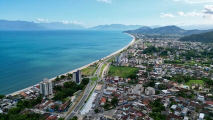 Linda vista aerea com drone sobre o mar com montanhas e cidade ao fundo com cores vibrantes.
