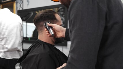 Skilled barber trimming client's hair using electric razor, creating contemporary hairstyle in modern barbershop setting with precise, professional technique