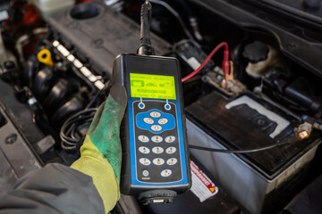 A mechanic uses a tester to diagnose a car battery by checking the voltage and performance for potential problems.