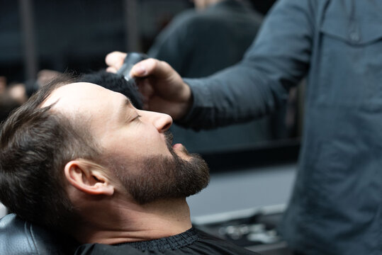 Skilled barber grooming client's beard using electric razor, delivering precise styling within contemporary barbershop setting
