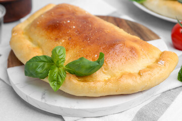 Tasty vegetarian calzone with basil on light table, closeup