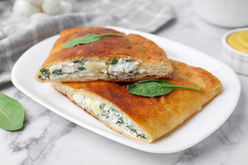 Pieces of tasty calzone with cheese and basil on white marble table, closeup