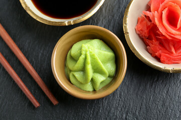 Hot wasabi paste, soy sauce, ginger and chopsticks on dark textured table, flat lay