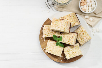 Delicious puffed rice bars, mint and candies on white wooden table, flat lay. Space for text