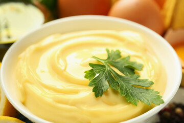 Delicious mayonnaise sauce with parsley in bowl and ingredients on table, closeup