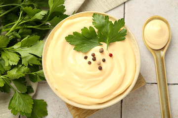 Delicious mayonnaise sauce with parsley, peppercorns in bowl and spoon on tiled table, flat lay