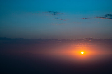 The sky is blue and the sun is setting. The sun is orange and the sky is clear