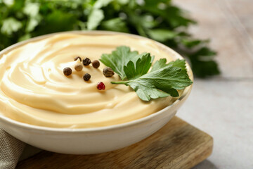 Delicious mayonnaise sauce with parsley and peppercorns in bowl on light table, closeup