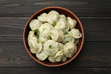 Tasty dumplings with green onion and dill in bowl on wooden table, top view
