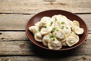 Tasty dumplings with green onion on wooden table, closeup. Space for text
