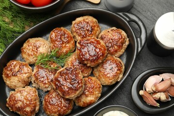Delicious patties in baking dish and spices on black table, flat lay
