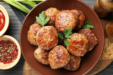 Delicious patties and spices on black textured table, flat lay
