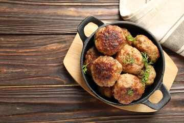 Tasty patties and dill in frying pan on wooden table, top view. Space for text