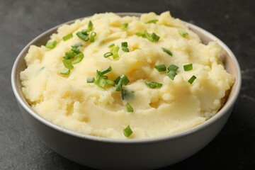 Delicious mashed potato with green onions in bowl on black table, closeup