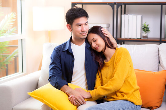 Portrait young asian couple hold hands sitting on sofa looking affectionate and embrace in living room at home, husband and wife with gentle and relation with cozy and love, couple and lifestyle.