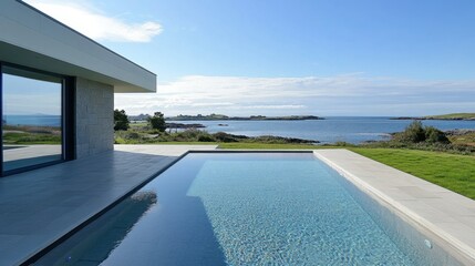 Obraz premium A modern infinity pool overlooking the sea, with large windows and flat roof tiles. The light grey limestone floor leads to a grassy lawn, showcasing the contemporary architecture