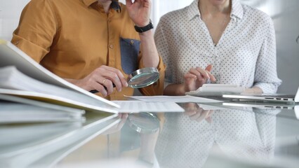 Two accountants conducting a financial audit in their office, closely examining documents with a magnifying glass and calculator. Taxes, audit in business