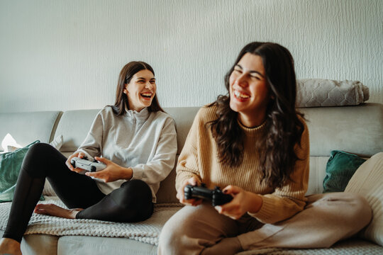 Young caucasian woman and her sister play video games on joystick and eat pizza