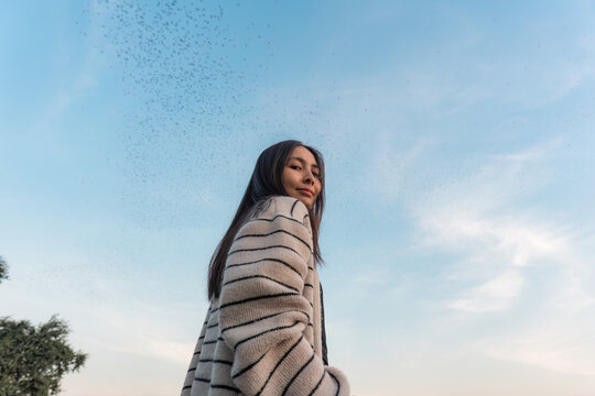 Asian woman smiling and enjoying with flock of bats flying in blue sky during the evening