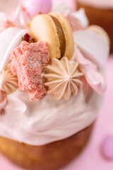 Traditional Ukrainian easter bread or sweet paska bread with topping decorated with cream and colorful meringue, macarons and eggs isolated on pink 