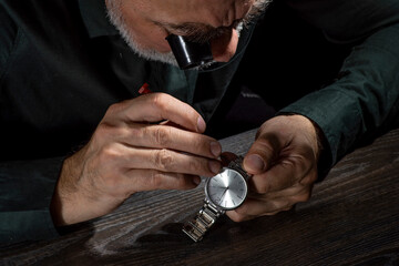 Watchmaker repairing watches looking through magnifying glass monocular. Professional senior watch fixer in repair services workshop.