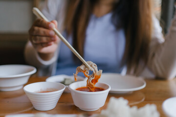 Close-up of a hand dipping sliced meat into spicy sauce using chopsticks. Traditional Asian hotpot dining experience, rich in flavors and culture. Perfect for food, lifestyle, and culinary themes.