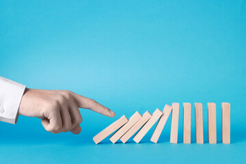 Domino effect. Man pushing wooden blocks on light blue background, closeup