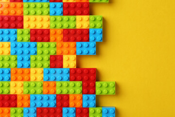 Constructor toy. Many colorful building blocks on yellow background, top view. Space for text