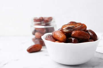 Tasty dried dates in bowl and jar on white marble table, closeup. Space for text