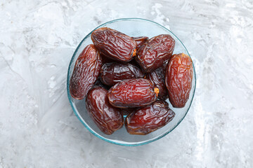Many tasty dried dates in bowl on gray textured table, top view